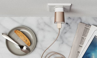 a wall charger plugged in on a granite counter top with papers and a plate with food on it